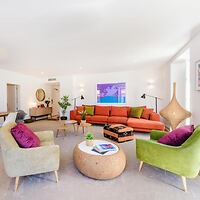 Spacious and stylish living room with a mix of mid-century and modern furniture, including a vibrant orange sofa and green armchairs