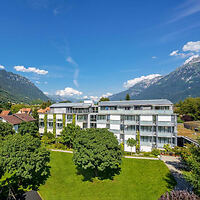 Aerial view of the Hotel Artos Interlaken, showcasing its modern architecture surrounded by well-kept gardens with the Swiss Alps in the background