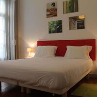 Minimalist bedroom with a bright red headboard, white bedding, and wall-mounted photographs