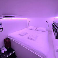 a cozy hotel room bathed in purple light, featuring a neatly made bed with white linens and reading lights