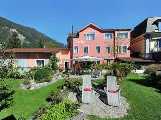 a charming pink hotel building with a green lawn and relaxation chairs, set against the backdrop of the Swiss Alps