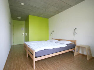 a hotel bedroom with a double bed with grey bedding and a green accent wall