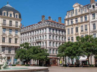 A picturesque view of a tree-lined plaza in Lyon with traditional French architecture where the hotel is located