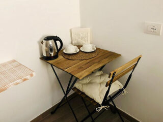 A cozy and minimalist bed and breakfast corner with a small wooden folding table, a black director's chair, and a white electric kettle on top