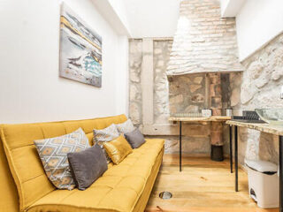 Cozy apartment living space in Porto featuring a mustard yellow sofa, exposed stone wall, and abstract art, blending rustic charm with modern design