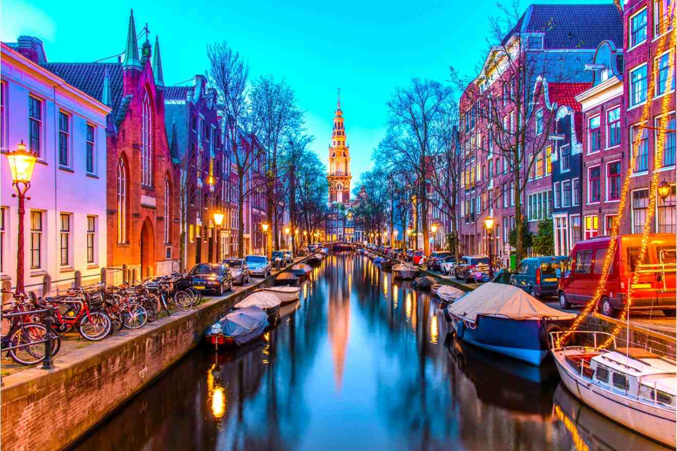 Twilight view of Amsterdam's canals with illuminated buildings and moored boats.