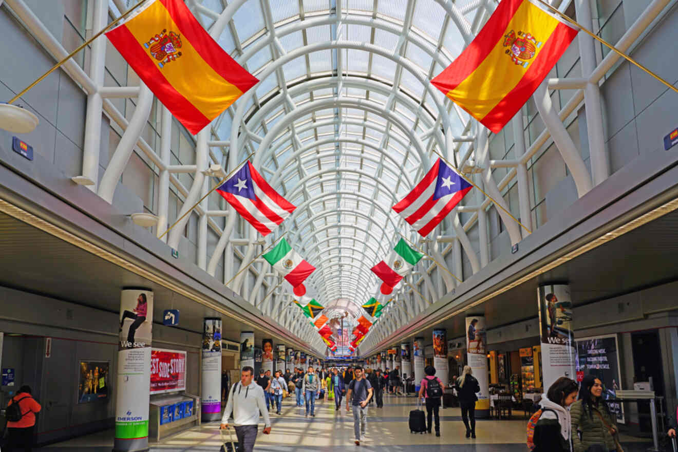 The interior of O’Hare International Airport in Chicago, adorned with a display of international flags, bustling with travelers beneath a geometric glass ceiling