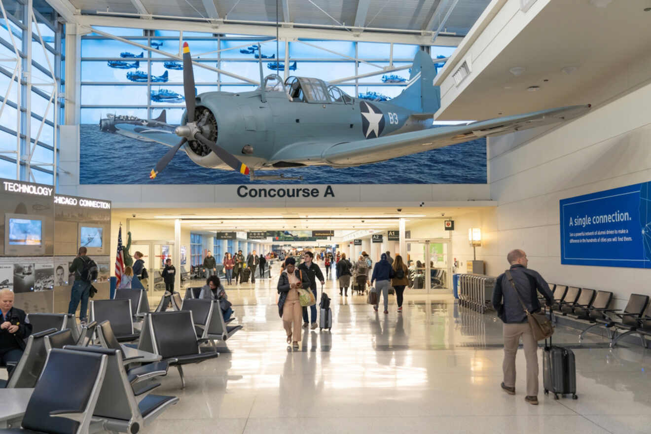 A World War II fighter plane exhibit hanging in the concourse of Midway International Airport in Chicago, with passengers and the American flag in the foreground