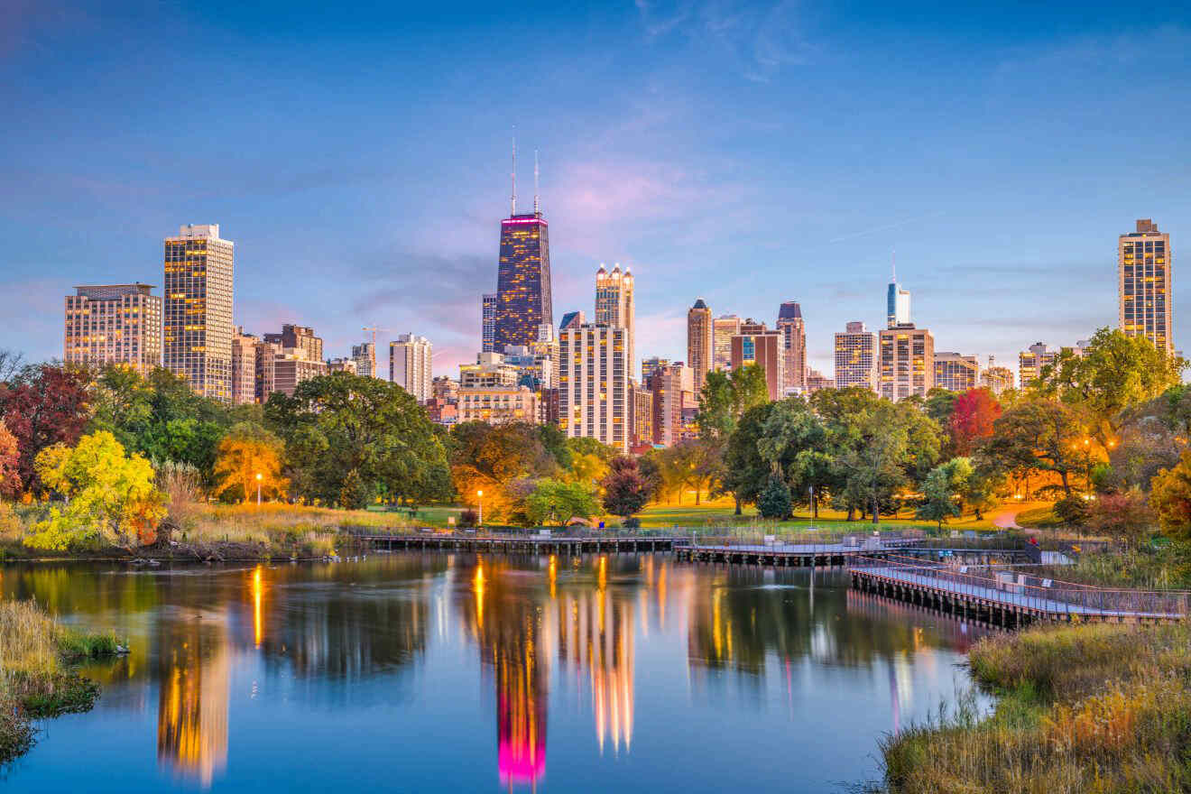 The Chicago skyline at twilight with the John Hancock Center standing tall, reflected on the serene waters of a park pond surrounded by autumn foliage