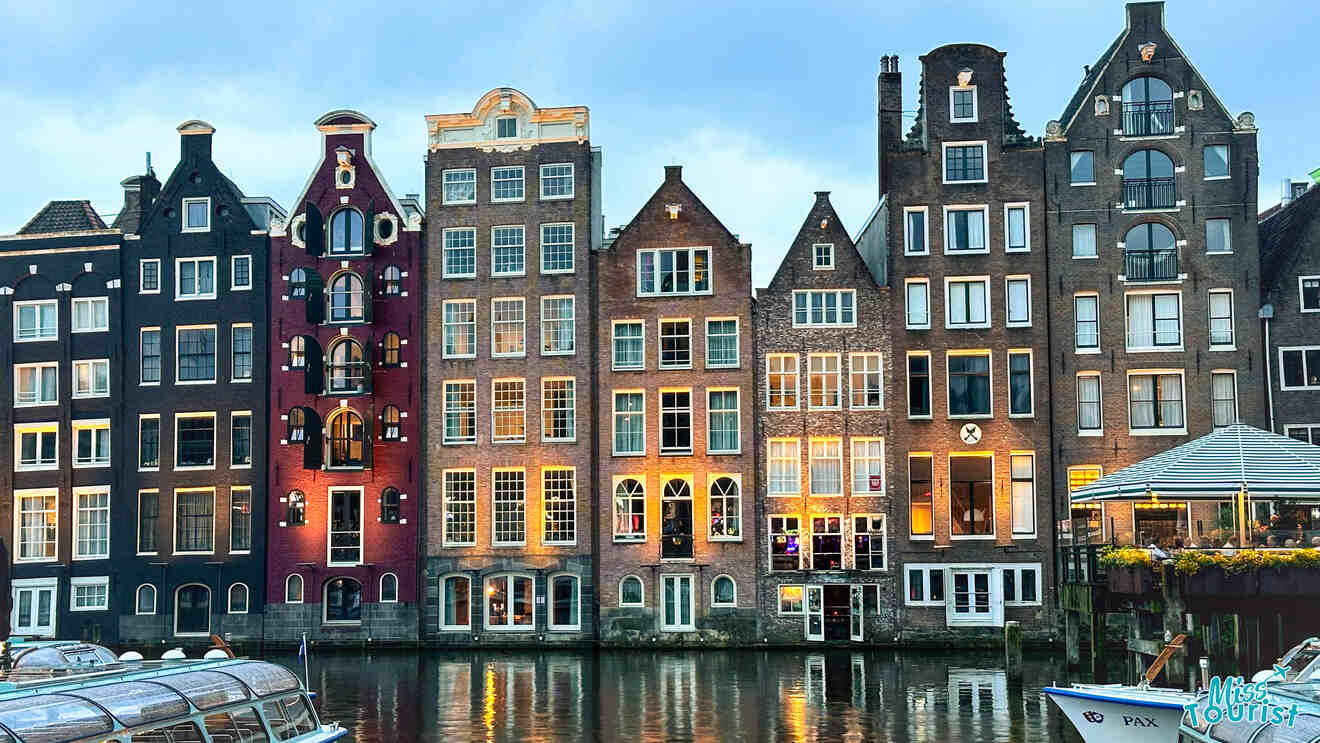 A row of tall, narrow, and colorful traditional Dutch houses reflecting in the calm canal water, showcasing Amsterdam's iconic canal belt.