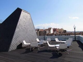 Rooftop terrace in Porto with white chairs set against a backdrop of unique architectural roof tiles and panoramic views of the city