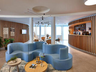 Curved blue modular sofas in a stylish hotel lobby with a circular wooden reception bar.