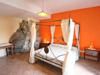 Bedroom with a four-poster bed, orange walls, a stone feature, and wooden furniture