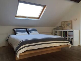 Simple attic bedroom with a large bed, skylight, and bookshelf, offering a cozy retreat