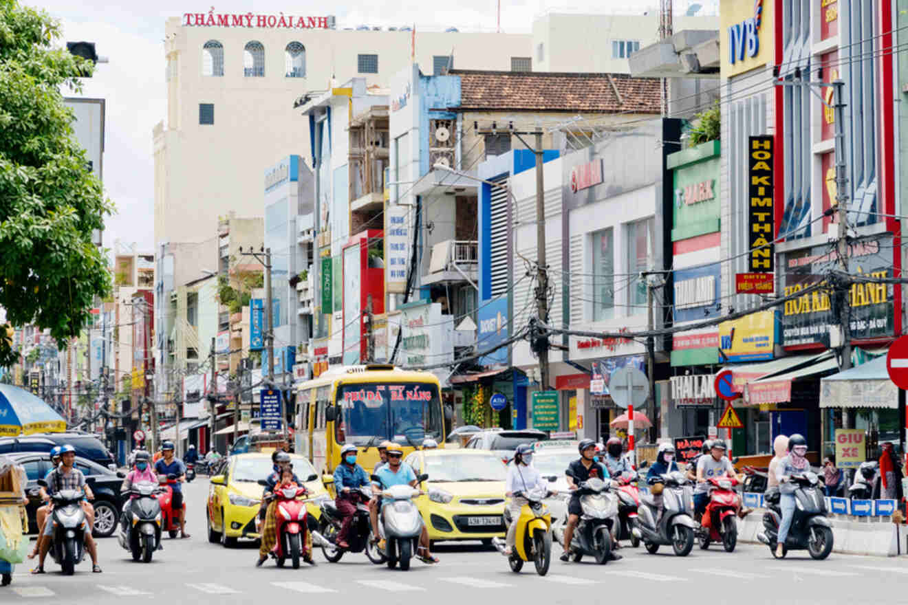 Vibrant street scene in Da Nang city center, with bustling traffic including motorcycles, cars, and a yellow city bus amidst colorful storefronts, highlighting the dynamic urban atmosphere