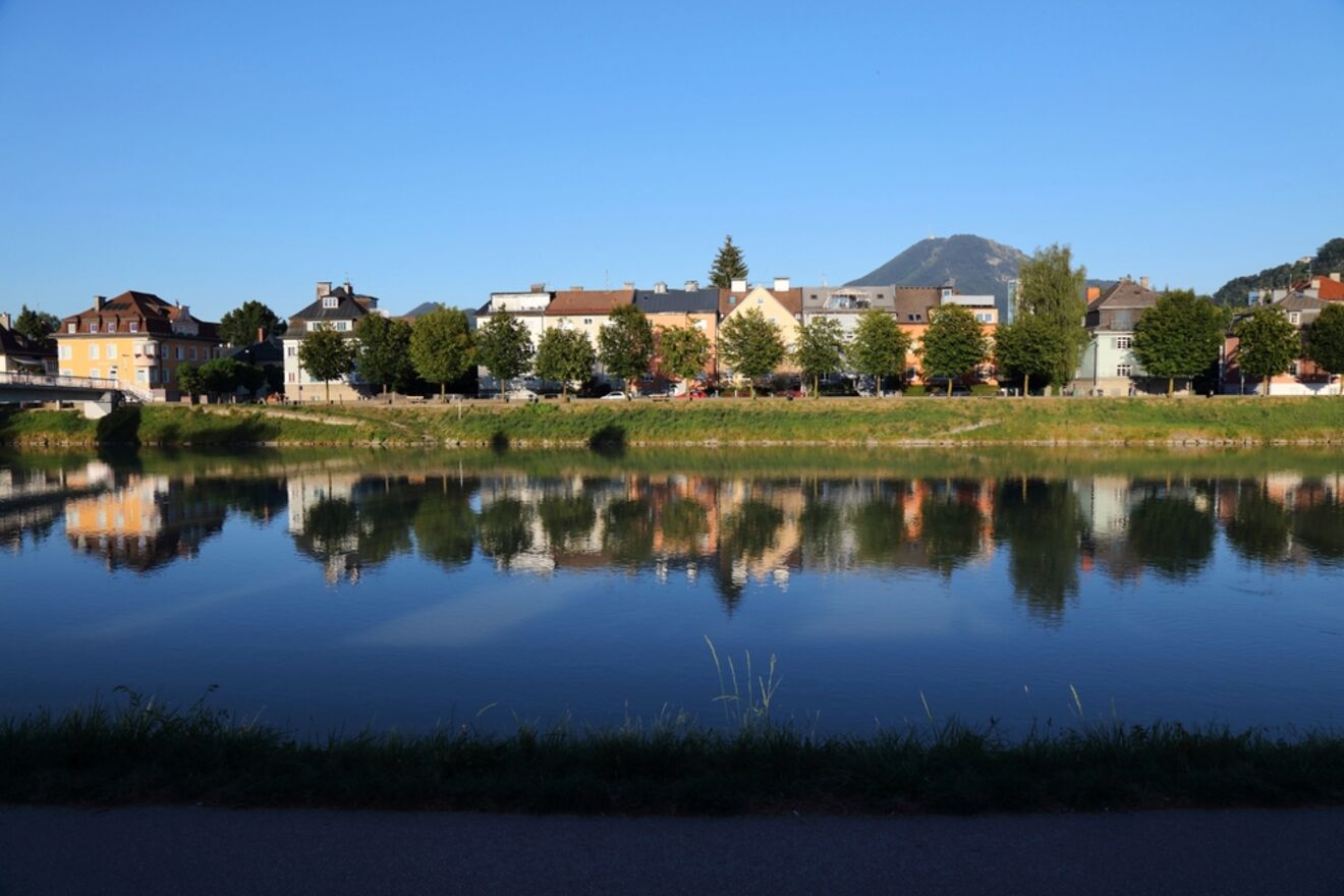 Calm river reflecting the picturesque houses and trees with a mountain in the background in Salzburg