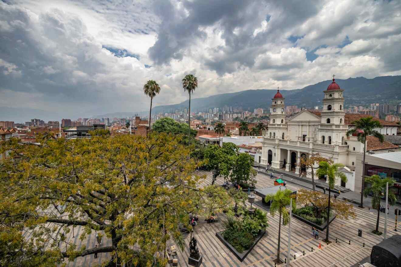 A breathtaking view of Medellín's historic church against a dramatic sky, framed by lush trees