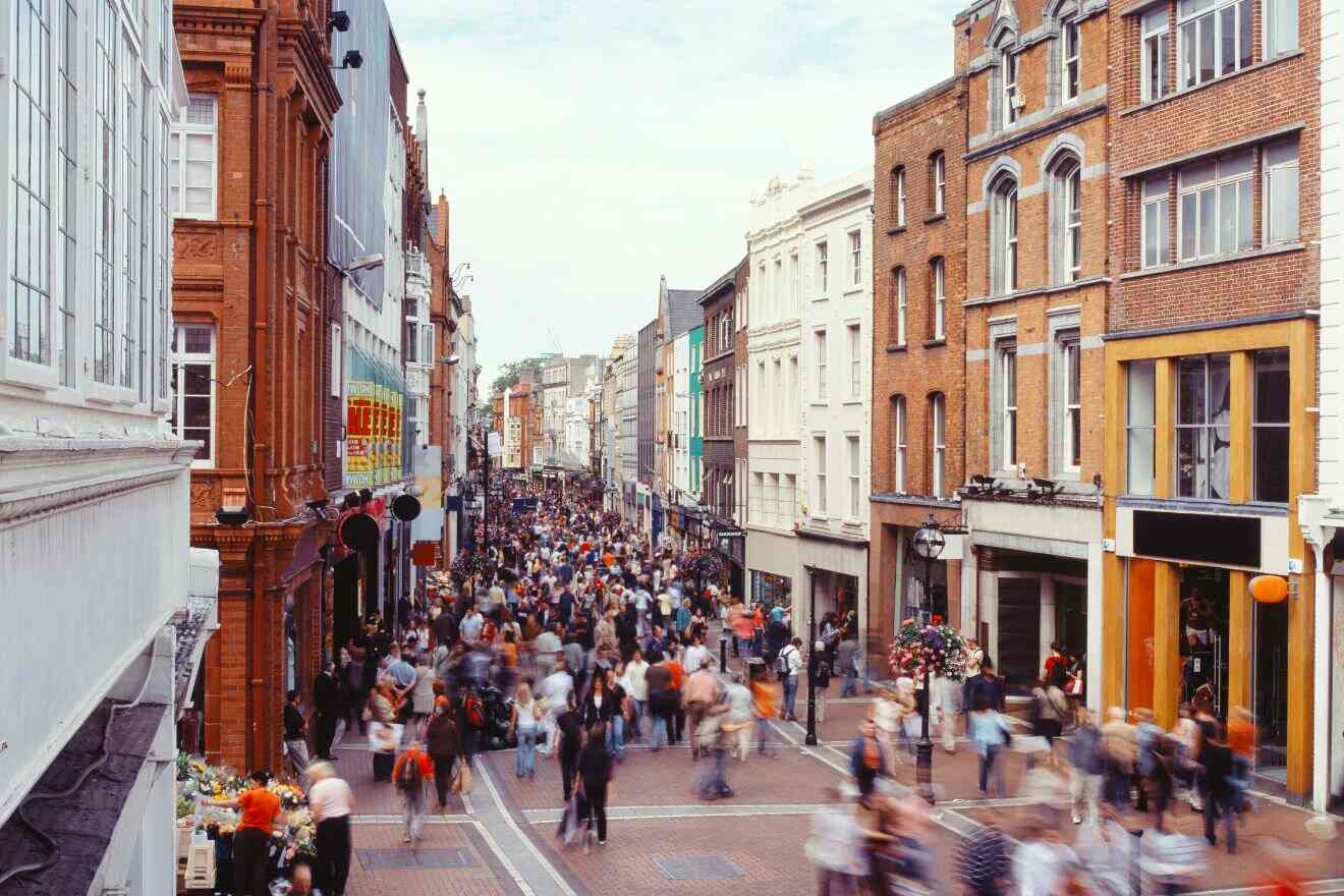A bustling Grafton Street in Dublin, with a crowd of shoppers and pedestrians, flanked by historic buildings under a soft white sky.