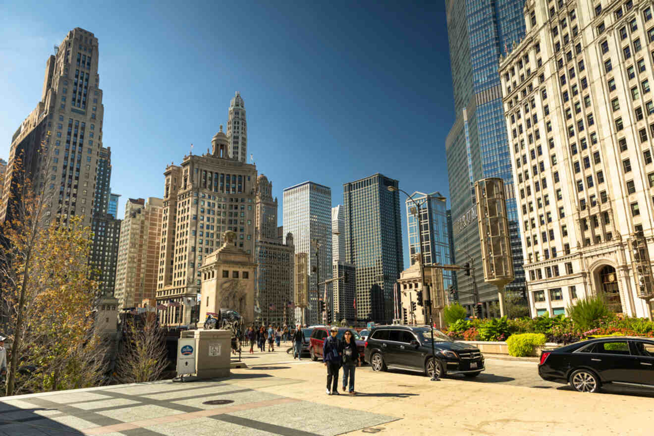 Pedestrians walking near Chicago's historic Wrigley Building, with its distinctive clock tower, amidst other skyscrapers on a clear day.