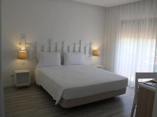 Modern hotel bedroom with a large bed, white bedding, and soft lighting