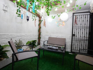 An intimate and decorative indoor patio with artificial grass flooring, string lights overhead, and simple outdoor furniture