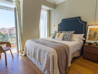 Elegant bedroom with a blue headboard, white bedding, decorative pillows, and a balcony overlooking the city
