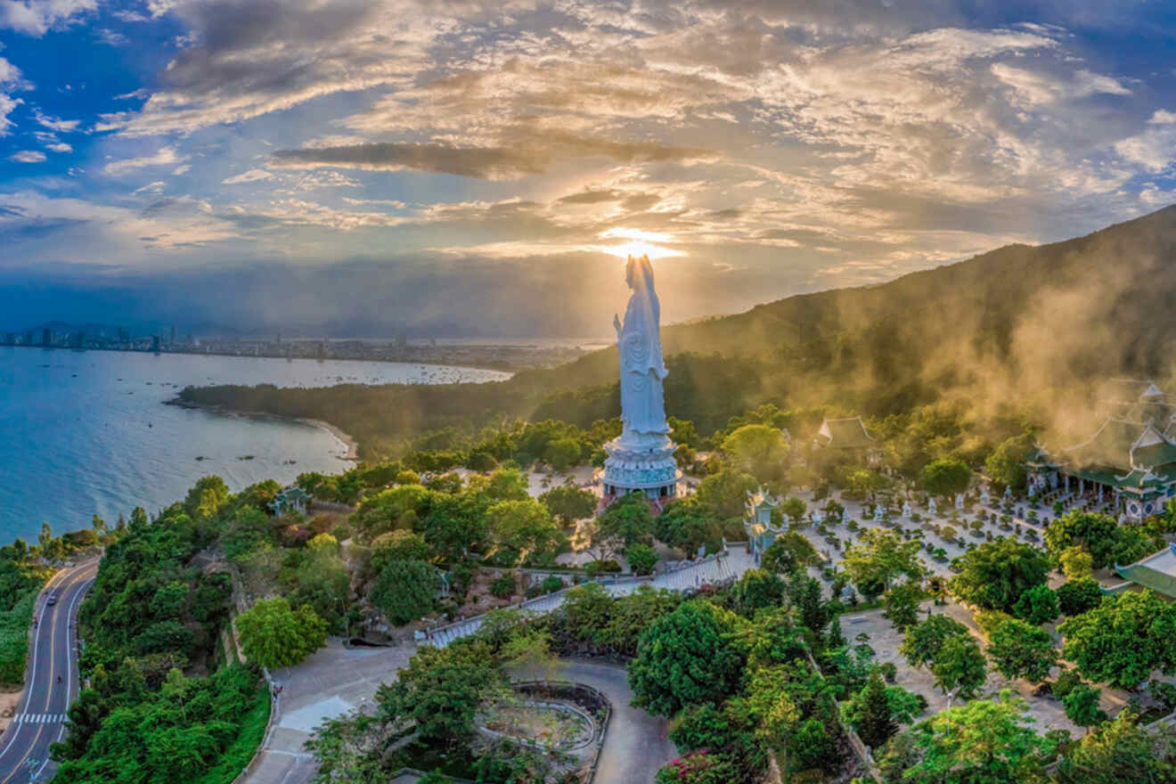 Breathtaking aerial view of the Lady Buddha statue at Son Tra Peninsula, Da Nang, as the sunset casts a warm glow over the serene landscape, highlighting the statue as a beacon above the surrounding lush greenery and calm bay waters