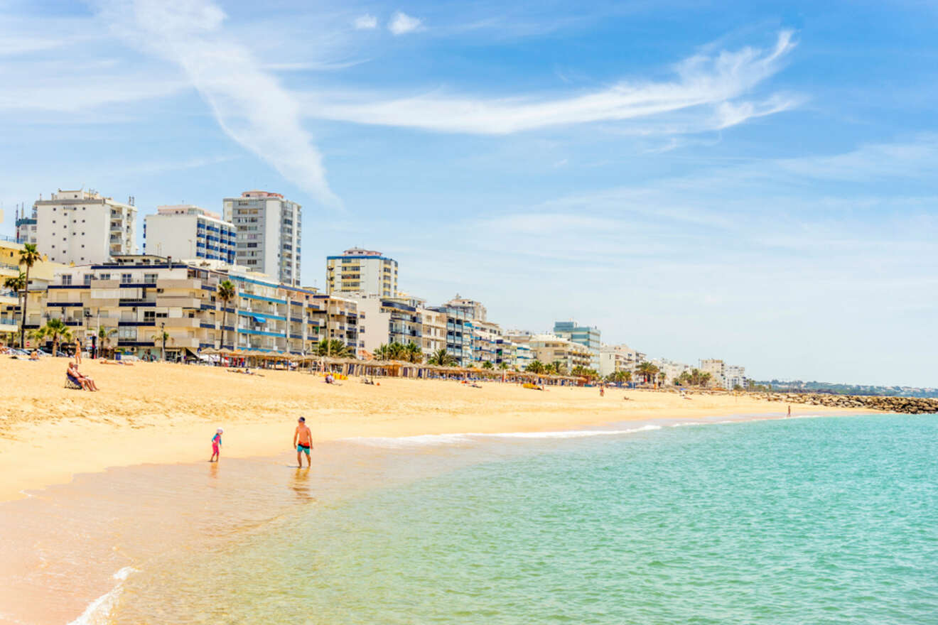 Sunny beach scene at Quarteira, Algarve, illustrating budget-friendly travel options with coastal apartments in the background