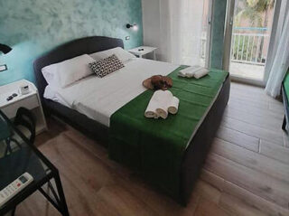 Hotel bedroom with a green headboard and bedding, white lampshades, and a balcony