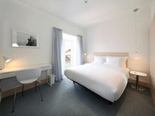 Bright bedroom with a minimalist design, featuring a double bed with white bedding and a modern desk by the window
