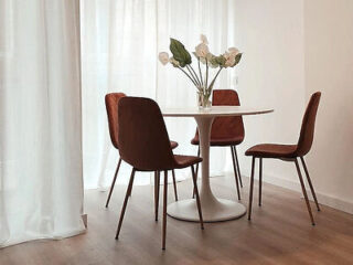 A modern dining area with a simple white round table, reddish-brown chairs, and minimalist decor