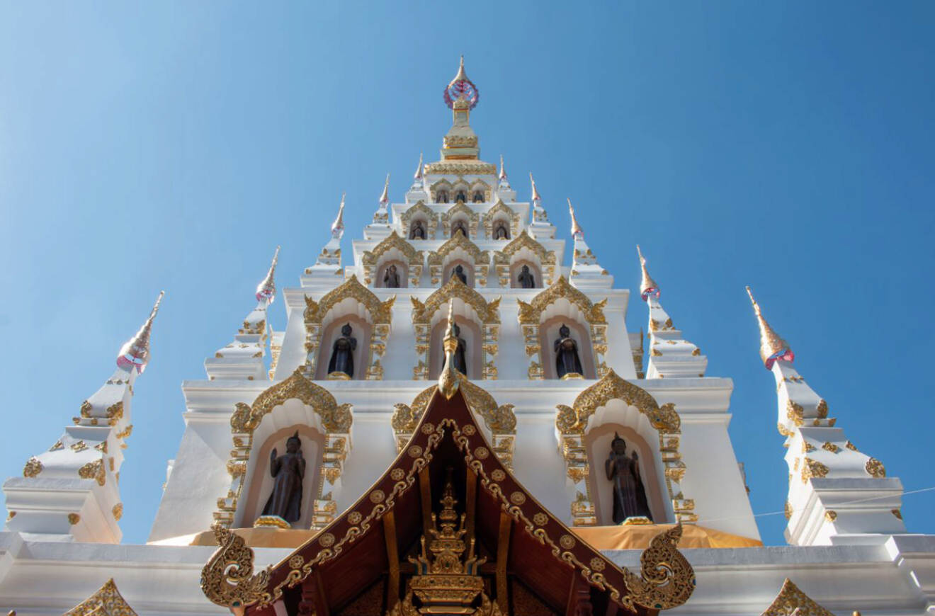 A striking view of a white and gold ornate temple in Chiang Mai, showcasing intricate architectural details against the backdrop of a clear blue sky.