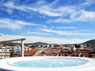 Jacuzzi on a rooftop terrace with a panoramic view of Nice, featuring clear blue skies and urban architecture, offering a luxurious relaxation spot