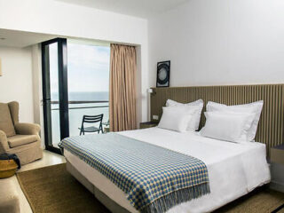 Hotel room with a king-sized bed, floor-to-ceiling window, and a balcony overlooking a scenic coastal view