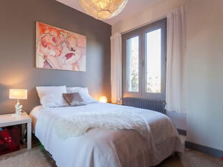An elegant bedroom with a large abstract painting above the bed, soft lighting, and neutral tones