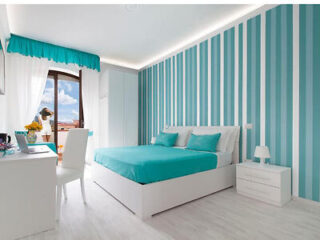 Bedroom with a teal and white striped wall, matching bedding, white furniture, and a balcony with a view