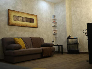 A comfortable living area with a brown sofa, a small bookshelf, ambient wall lighting, and a warm color palette