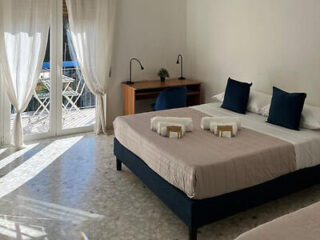 A bright and airy bedroom with a large bed, blue accent pillows, white sheer curtains, and a balcony