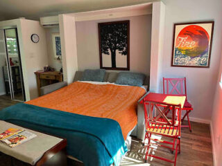 an apartment bedroom with orange and blue bedding, and a table with chairs next to it