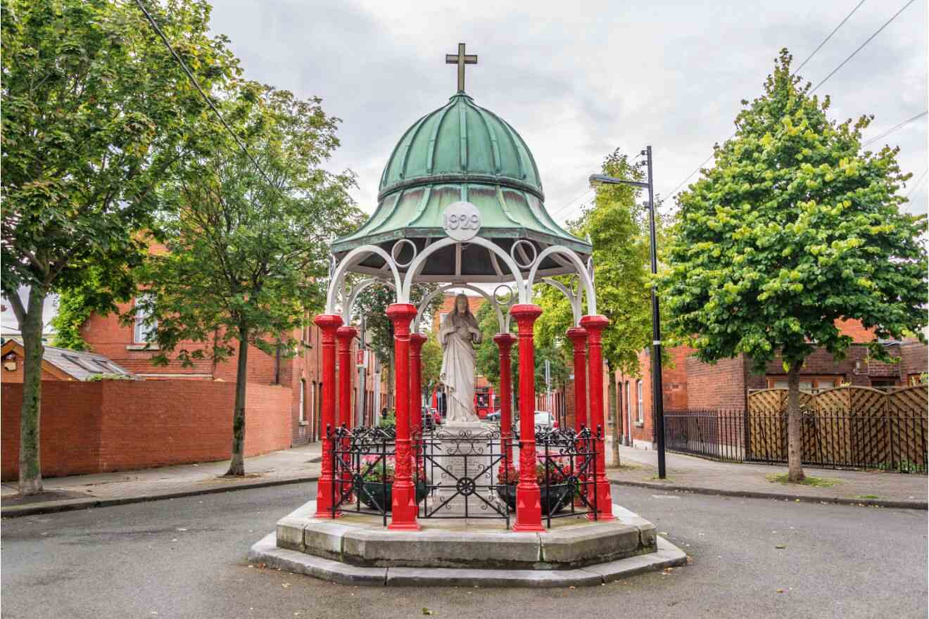 A bronze statue of a seated woman with a beaded hat, set against a backdrop of Georgian-style red brick buildings with white-trimmed windows and classic red doors in Dublin.