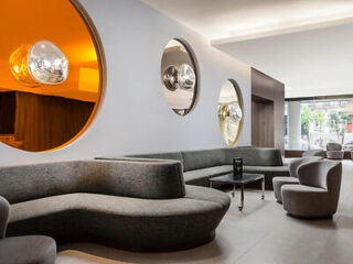 Modern hotel lobby in Porto with curvaceous dark grey sofas, round mirrors, and striking orange accents creating a chic and contemporary atmosphere