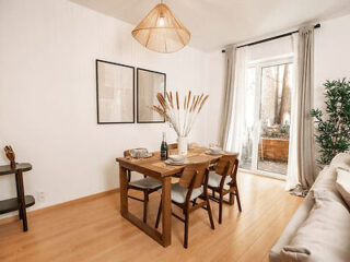 Dining area in a bright apartment with wooden furniture, a woven light fixture, and large windows