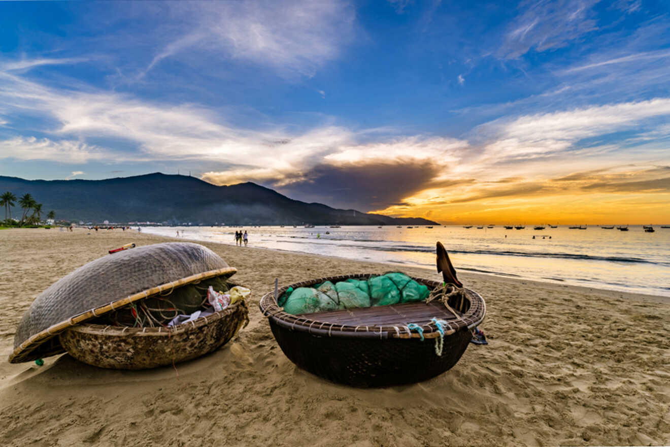 Traditional round bamboo boats on the sandy shore at sunset, with Da Nang's mountains silhouetted against a vibrant sky