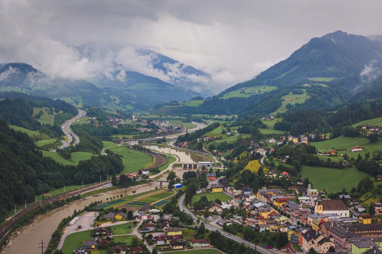 Overcast view of the Salzach Valley with a winding river, roads snaking through green fields, and Austrian villages nestled among forested hills, all shrouded in mist