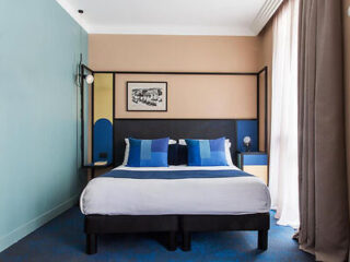 Elegant hotel room with a stylish black bed frame, blue accent cushions, and a contrasting tan wall