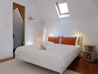 Attic bedroom with skylight, featuring a double bed with white linen and orange pillows, and a rustic wooden floor