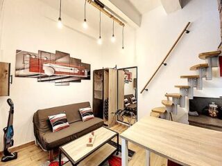 Compact and trendy studio space with a spiral staircase, minimalist furniture including a sofa bed and a dining table, accented with chic lighting and contemporary wall art