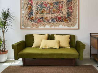 An inviting living area in a Porto townhouse, featuring a plush olive green sofa with yellow cushions, a decorative rug, and a large botanical art piece