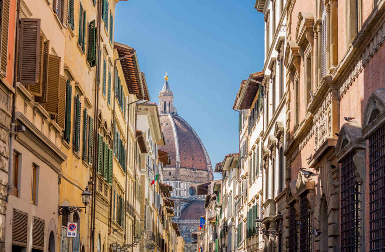A narrow street in Florence with traditional Italian buildings leading towards the majestic dome of the Cathedral of Santa Maria del Fiore in the background