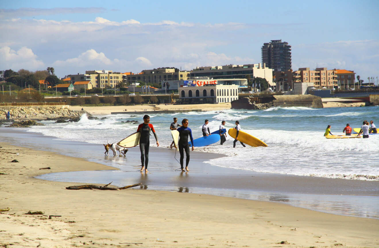 Surfers and beachgoers enjoy the sandy shores near Porto, with the city's seaside architecture in the background and waves rolling in from the Atlantic